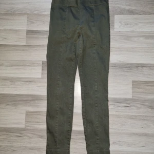 Olivgröna byxor från H&M, strl 40 - Snygga olivgröna byxor från H&M i storlek 40, docksmåistorleken. Byxorna har hög midja och raka ben med en enkel, stilren look. Tillverkade i ett mjukt bomullsmaterial med lite stretch för extra komfort. Perfekta för en chill och avslappnad stil.