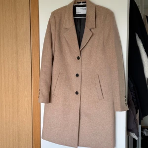 Beige kappa från Selected Femme - Snygg beige kappa från Selected Femme med klassisk krage och tre svarta knappar framtill. Jackan har raka fickor och knappar vid ärmsluten. Perfekt för dig som gillar stilrena och tidlösa plagg med en chill vibe. Använd en gång. Säljer då färgen inte passar mig. 