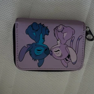 Lila Stitch plånbok med dragkedja - Söt lila plånbok med motiv av Stitch och Angel från Lilo & Stitch. Plånboken har dragkedja runtom och kortfack på baksidan. Perfekt för dig som älskar Disney och vill ha något unikt i väskan.