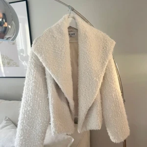 Vit teddyjacka från NA-KD - Supermysig vit teddyjacka från NA-KD med oversized krage och lång ärm. Jackan har en fluffig struktur och boxig passform som ger en chill vibe. Perfekt att slänga på sig när det är kallt ute och du vill vara både varm och snygg.