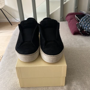 Svarta sneakers från Axel Arigato/ storlek 37 - Svarta slip-on sneakers från Axel Arigato med ovandel i mocka och bred resår över vristen. Skorna har en chunky vit platt sula och rund tå. Perfekta för en clean och stilren look. Pris diskuterbart 