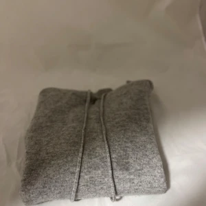 Grå hoodie i kashmir - Mjuk och stilren grå hoodie med huva och dragsnören. Tröjan är stickad i kashmirblandning och har ribbade muddar vid ärmslut och nederkant. Perfekt för dig som gillar en clean och avslappnad look.