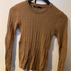 Beige kabelstickad tröja Gina Tricot - Säljer en beige kabelstickad tröja från Gina Tricot. Tröjan har rund halsringning, lång ärm och ribbade muddar. Perfekt för lager-på-lager och enkel att matcha med jeans eller kjol.