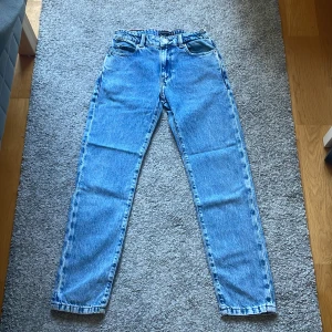 Blå jeans från Tommy Hilfiger - Klassiska blå jeans från Tommy Hilfiger i rak modell. Jeansen har fem fickor, normal passform och är tillverkade i slitstarkt bomullsjeans. Snygga kontrastsömmar och läderpatch bak i midjan. Perfekta till en avslappnad stil.