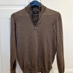 Brun merinoulltröja med half zip från Sand - Brun långärmad tröja från Sand Copenhagen i mjuk och extrafin merinoull. Tröjan är i mycket bra skick. Tröjan har en stilren ståkrage med half zip-dragkedja framtill och ribbade muddar vid ärmslut och nederkant. Nypris:2000 kr 