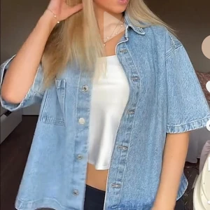 Oversized ljusblå jeansskjorta - Säljer en oversized ljusblå jeansskjorta med korta ärmar och stor bröstficka. Skjortan har klassisk krage och knappar framtill. Perfekt att slänga över en crop top för en chill och trendig look. Materialet är kraftigt denim och passformen är loose.💗💗