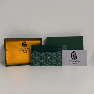 Grön G yard plånbok med mönster - Snygg grön plånbok från G yard med ikoniskt grafiskt mönster i vitt och beige. Plånboken är tillverkad i skinn och canvas, har flera kortfack och levereras med originalask och dustbag. Perfekt för dig som vill ha något exklusivt och stilrent i fickan.