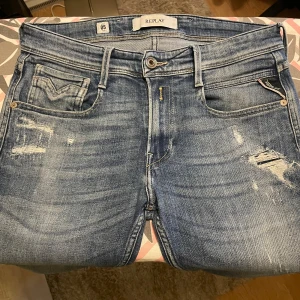 Ljusblåa Replay Anbass  - Tjena! Jag säljer just nu mina tvärsnygga Replay Anbass jeans i blå tvätt med slitningar och distressed detaljer. Slim fit klassisk knapp och dragkedja. Märkespatch bak i brunt läder. W29 L32! Hör av er vid frågor eller funderingar! 🤩