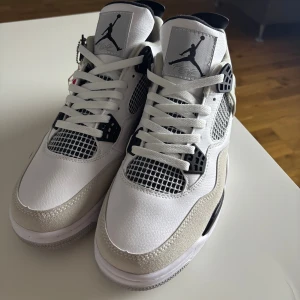 Nike Air Jordan 4 vit/svart sneakers - Nike Air Jordan 4 sneakers i vit och svart med grå mockadetaljer. Klassisk siluett med meshpaneler, snörning och Jumpman-logga på plösen. Skorna har platt sula och rund tå, tillverkade i skinn och mocka för en clean vibe.  Priset går verkligen att diskuteras.
