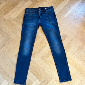 Mörkblå slim jeans från Jack & Jones - Snygga mörkblå slim jeans från Jack & Jones med klassisk femficksdesign och diskreta slitningar. Jeansen har normal midja och är tillverkade i stretchig denim för en bekväm passform. Perfekta för dig som gillar en smal siluett och stilren look. Hör av er vid frågor