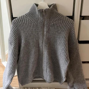 Grå ribbad kofta från BikBok - Säljer en grå ribbstickad kofta från BikBok i storlek XS. Koftan har hög krage och hel dragkedja framtill.