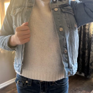 Ljusblå jeansjacka med knappar - Snygg ljusblå jeansjacka med klassisk krage och silverfärgade knappar framtill. Jackan har två bröstfickor med lock och långa ärmar. Perfekt att slänga på över en hoodie eller t-shirt för en chill look.