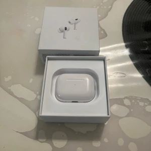 AirPods Pro 2 2023 - Apple AirPods Pro 2 2023 med originalförpackning och laddningskabel. Fodralet och tillbehören ser ut att vara i gott skick. Aktiv brusreducering och trådlös laddning. Perfekt för musik och samtal. Kvitto finns också!