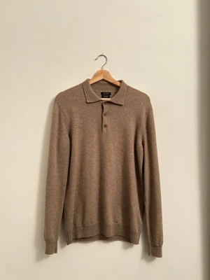 Beige kashmirpiké från Massimo Dutti - Snygg beige pikétröja från Massimo Dutti i mjuk kashmirmix. Klassisk krage och tre knappar framtill, långärmad och med ribbade muddar. Perfekt för dig som gillar stilrena och sköna plagg med lyxig känsla.