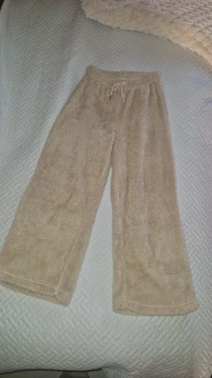 Fluffiga mjukisbyxor - Supermysiga beiga mjukisbyxor i fluffigt fleece-material. Vida ben och elastisk midja med snörning för extra komfort. Perfekta för chill dagar hemma eller när du vill vara extra cozy. Inga defekter