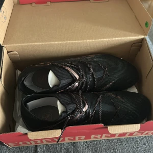 Puma Future 7 Ultimate fotbollsskor - Säljer ett par Puma Future 7 Ultimate FG/AG fotbollsskor i svart och kopparrosa. Skorna har snörning, platt sula med dobbar och ett snyggt mönster med kopparfärgade detaljer. Ovandelen är i syntetmaterial och designen är riktigt modern och sportig. Helt nya inte använda någon gång, hör av er vid funderingar// William 