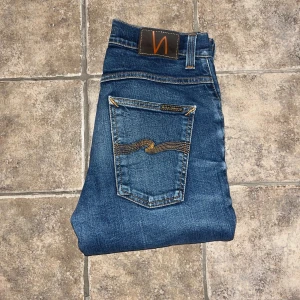 Nudie Jeans Grim Tim  - Snygga blå jeans från Nudie Jeans, modellen Grim Tim.  Jeansen är raka och har normal passform, tillverkade i 98% ekologisk bomull och 2% elastan för extra komfort. OBS se blekning på vänster framficka . Midja 36cm, längd 113cm. JAG SKICKAR EJ FLER BILDER NÄR JAG BÄR JEANSEN! för storleksguide hänvisar jag till måtten och för bättre inblick i passformen rekommenderar jag att googla på modellnamnet. :) S4