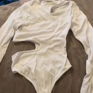 Vit ribbad långärmad topp med cut-outs - Säljer en vit ribbad långärmad topp med coola cut-outs vid axel och midja. Toppen har en slim passform och är tillverkad i mjuk bomull som sitter skönt mot kroppen. Perfekt för dig som gillar trendiga detaljer och vill sticka ut lite extra. Pris kan diskuteras och köparen står för frakt