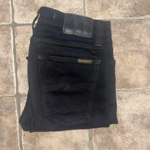 Nudie Jeans  - Svarta jeans från Nudie Jeans, modellen High Kai. De har en slim och skinny passform med hög midja. Materialet är 98% ekologisk bomull och 2% elastan för extra stretch. Midja 37cm, längd 108cm. JAG SKICKAR EJ FLER BILDER NÄR JAG BÄR JEANSEN! för storleksguide hänvisar jag till måtten och för bättre inblick i passformen rekommenderar jag att googla på modellnamnet. Jeansen kan vara uppsydda utan att jag noterat det så kolla måtten noggrant :) s4 