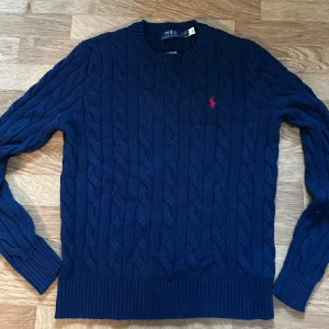 Marinblå kabelstickad tröja Polo Ralph Lauren - Säljer en stickad marinblå tröja från Polo Ralph Lauren. Jag fick denna tröja n i present  men den var tyvärr i fel storlek och jag har inte möjligheten att fråga om kvittot. Tröjan är i nyskick som ni ser själva! Om det inte var allt ni ville veta finns jag här i Plick att skriva till. Pris och allt annat kontaktas genom privat! MVH Robin