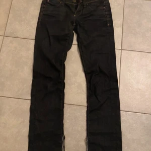 Svarta  jeans från ONLY - Svarta jeans från ONLY Limitless-serien med skinny fit och klassiska kontrastsömmar och en låg midja. Jeansen har fem fickor, dragkedja och knapp framtill samt snygga detaljer på bakfickorna. Perfekta för dig som gillar en tight och stilren look. Har dock klippt upp vid sidorna vid benen så dom är mer stright/bootcut