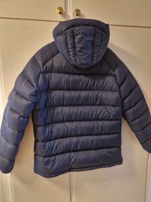 Mörkblå dunjacka Peak Performance Large - Säljer en mörkblå dunjacka från Peak Performance med huva och snygg quiltad design. Jackan har dragkedja framtill och två sidofickor med dragkedja. Perfekt för kalla dagar och har en stilren look som funkar till det mesta.