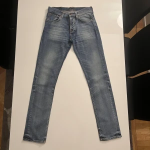 Blå jeans från Nudie Jeans - Säljer ett par snygga blå jeans från Nudie Jeans i storlek 31/34. modellen är runt 180 lång och väger runt 68kg. De har klassisk femficksdesign, orangea sömmar och Nudie-logga på bakfickan. Jeansen har en slim passform och är tillverkade i mjukt denim med lätt slitning för en cool look.