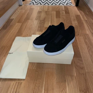 Svarta sneakers från Axel Arigato - Snygga svarta sneakers från Axel Arigato i mocka med vit platt sula och diskret guldfärgad logga på sidan. Stilren design utan snörning, perfekt för dig som gillar minimalistiska och trendiga skor. Levereras med originalkartong och dustbag. Skorna är använda upp emot 10 gånger men är väldigt väl omhändertagna och rena och fina i sin helhet.