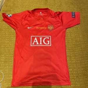 Manchester United 2008 Ronaldo tröja - Manchester Uniteds officiella Champions League-finaltröja från 2008 med Ronaldo 7 på ryggen. Röd med vita detaljer, AIG sponsortryck, klubbmärke och Nike-logga. Champions League- och Respect-patchar på ärmarna. Tillverkad i polyester.