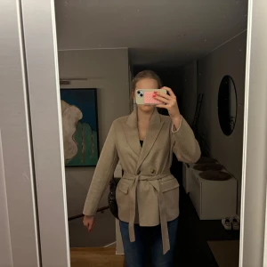 Beige kappa från Selected Femme - Jättesnygg beige kavajjacka från Selected Femme!!💗Jackan har bälte och fickor, och är perfekt för hösten eller våren. Knappt använd