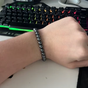 Grått pärlarmband med metallisk look - Snyggt armband med runda pärlor i grå metallisk färg. Pärlorna är jämnt fördelade på ett elastiskt band som gör det enkelt att ta på och av. Perfekt för dig som gillar minimalistisk och stilren design.