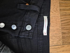 Levi's Wedgie Straight svarta jeans - Svarta jeans från Levi's i modellen Wedgie Straight. Klassisk femficksdesign med raka ben och hög midja. Jeansen har silverfärgade knappar och är tillverkade i bomull med en liten del elastan för extra komfort. Perfekt för dig som gillar en clean och tidlös look.