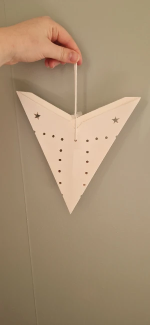 Adventsstjärna med hålmönster - Stilren vit lite mindre pappersstjärna med stansade stjärnor och prickar. Hängs upp med medföljande snöre. En liten fläck syns på en spets- ej provat få bort annars i gott skick.