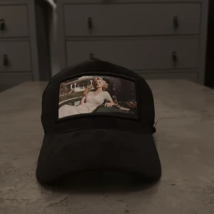 Svart keps från Maggiore - Svart keps från Maggiore med meshpaneler på sidorna och baksidan för extra ventilation. Framtill finns en stor patch med ett retroinspirerat foto och diskret Maggiore-logga. Justerbar passform baktill och metallogo på sidan. Perfekt för en cool streetstyle-look.