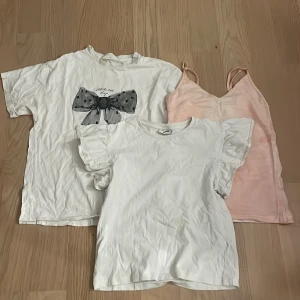 3-pack toppar från H&M, Kappahl & 157 - Säljer tre snygga toppar: en vit t-shirt från H&M med stor svart rosett framtill, en vit volangtopp från Kappahl och ett ljusrosa linne från 157 med smala axelband. Perfekta för att mixa och matcha till olika outfits.🩷