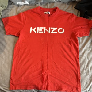 Röd Kenzo t-shirt med logga - Röd t-shirt från Kenzo med stor vit logga framtill. Klassisk rund halsringning och korta ärmar. Tillverkad i mjuk bomull för en skön känsla. Perfekt för dig som vill sticka ut med en enkel men snygg look.