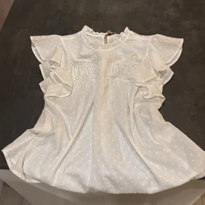 Vit blus med spets från Vero Moda - Supersöt vit blus från Vero Moda i 100% ekologisk bomull. Blusen har volangärmar, spetsdetaljer över bröstet och ett diskret prickigt mönster. Rund halsringning med liten volangkant och luftig passform. Perfekt för dig som gillar romantisk och fräsch stil.💞💞