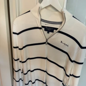 Vit randig half zip-tröja Bondelid - Snygg vit tröja från Bondelid med svarta horisontella ränder och half zip-dragkedja vid halsen. Tröjan har lång ärm, ribbad krage och är gjord i mjuk bomull. Perfekt för dig som gillar klassisk och stilren look.