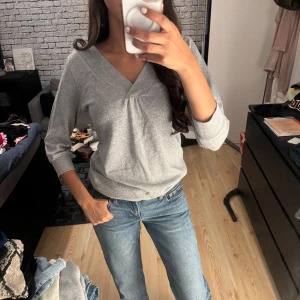 Glittrig silvertröja  - Säljer en snygg glittrig silverfärgad tröja från Amisu i storlek S. Tröjan har bred v-ringad hals, ribbade muddar och trekvartsärm. Knappt använd- som ny 