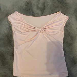 Ljusrosa ärmlös topp med twist - Supersöt ljusrosa topp med twistad detalj framtill. Toppen är ärmlös och har en mjuk, stretchig känsla som gör den bekväm att bära. Perfekt för dig som gillar en feminin och enkel stil.