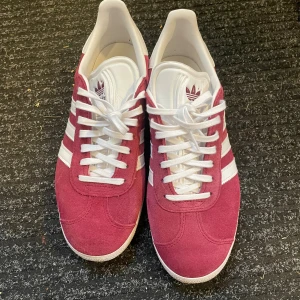 Adidas Gazelle vinröda sneakers mocka - Säljer ett par Adidas Gazelle sneakers i vinröd mocka med vita detaljer! Använda ca. 3ggr säljes då dem är lite för små för mig