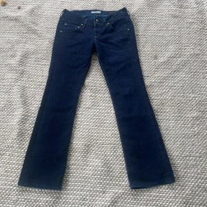 Mörkblå bootcut jeans från Lee - Snygga mörkblå jeans från Lee med klassisk femficksdesign och bootcut-ben. Jeansen har låg midja och är tillverkade i stretchig denim för en bekväm passform. Perfekta för dig som gillar en tidlös och stilren look. Midjemått ca 39 cm innerbenslängd ca 80 cm