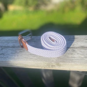 Vitt flätat bälte med skinn-detaljer - Snyggt vitt flätat bälte med bruna skinn-detaljer och silvrigt spänne. Bältet är cirka 100 cm långt och har en stilren look som passar till jeans eller shorts. Perfekt accessoar för att lyfta din outfit med en fräsch och modern touch.