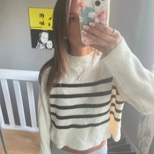 Vit och svart randig stickad tröja - Säljer en vit stickad tröja med svarta horisontella ränder. Tröjan är croppad med lång ärm och har en lite högre hals. Den är ribbstickad och har en loose fit, perfekt för en chill och stilren look.