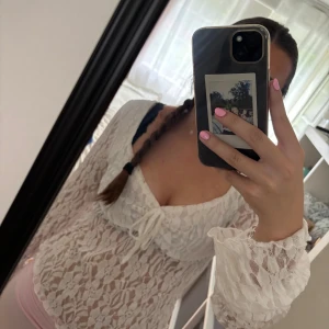 Vit spetsblus med knyt framtill - Säljer en romantisk vit blus i spets med långa ärmar och söt knytning framtill. Blusen är genombruten och har en feminin v-ringning. Perfekt för dig som gillar en söt och trendig stil.