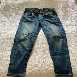 Blå jeans från The Blue Uniform - Snygga blå jeans från The Blue Uniform med klassisk femficksdesign och knäppning med flera knappar. Jeansen har en rak passform och är tillverkade i slitstarkt denimtyg med snygga slitningar och kontrastsömmar. Perfekta för en avslappnad och cool stil.