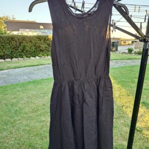 Svart ärmlös klänning från H&M Divided - Snygg svart klänning från H&M Divided i storlek 34. Modellen är ärmlös med rund hals och har en markerad midja som ger en fin siluett. Klänningen är kort och har en dragkedja i ryggen för enkel påklädning. Perfekt för dig som gillar enkel och stilren design.
