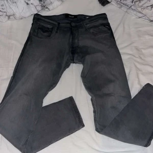 Replay grå jeans  - Snygga grå jeans från Replay med klassisk femficksdesign och raka ben. Jeansen har svarta detaljer på fickorna och en diskret Replay-logga. Tillverkade i mjukt denimtyg som sitter skönt hela dagen.