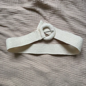 Skärp med stretch  -  midjebälte i vävt material med ett runt spänne som också är klätt i tyg. Storlek xs/s ca 60-70cm