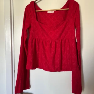 Röd blus med spets från Nelly - Supersöt röd blus från Nelly med långa klockformade ärmar och fyrkantig urringning. Peplummodell med spetsmönster, väldigt romantisk. Prislappen kvar, aldrig använd. Säljer också en likadan i mörkblått! Passar s/m.